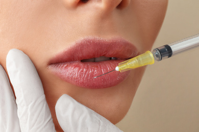 Woman getting lip injection on beige background, closeup