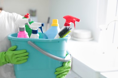 Photo of Woman holding bucket with cleaning supplies in kitchen, closeup