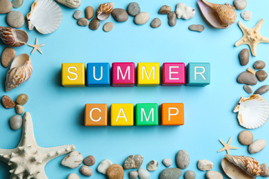 Colorful wooden cubes with phrase SUMMER CAMP on light blue background, flat lay