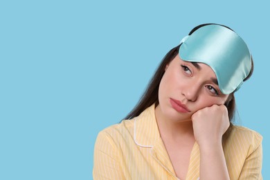 Tired young woman with sleep mask on light blue background, space for text. Insomnia problem