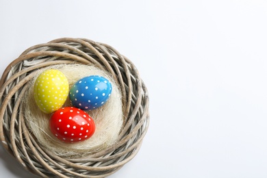 Wicker nest with painted Easter eggs on white background, top view