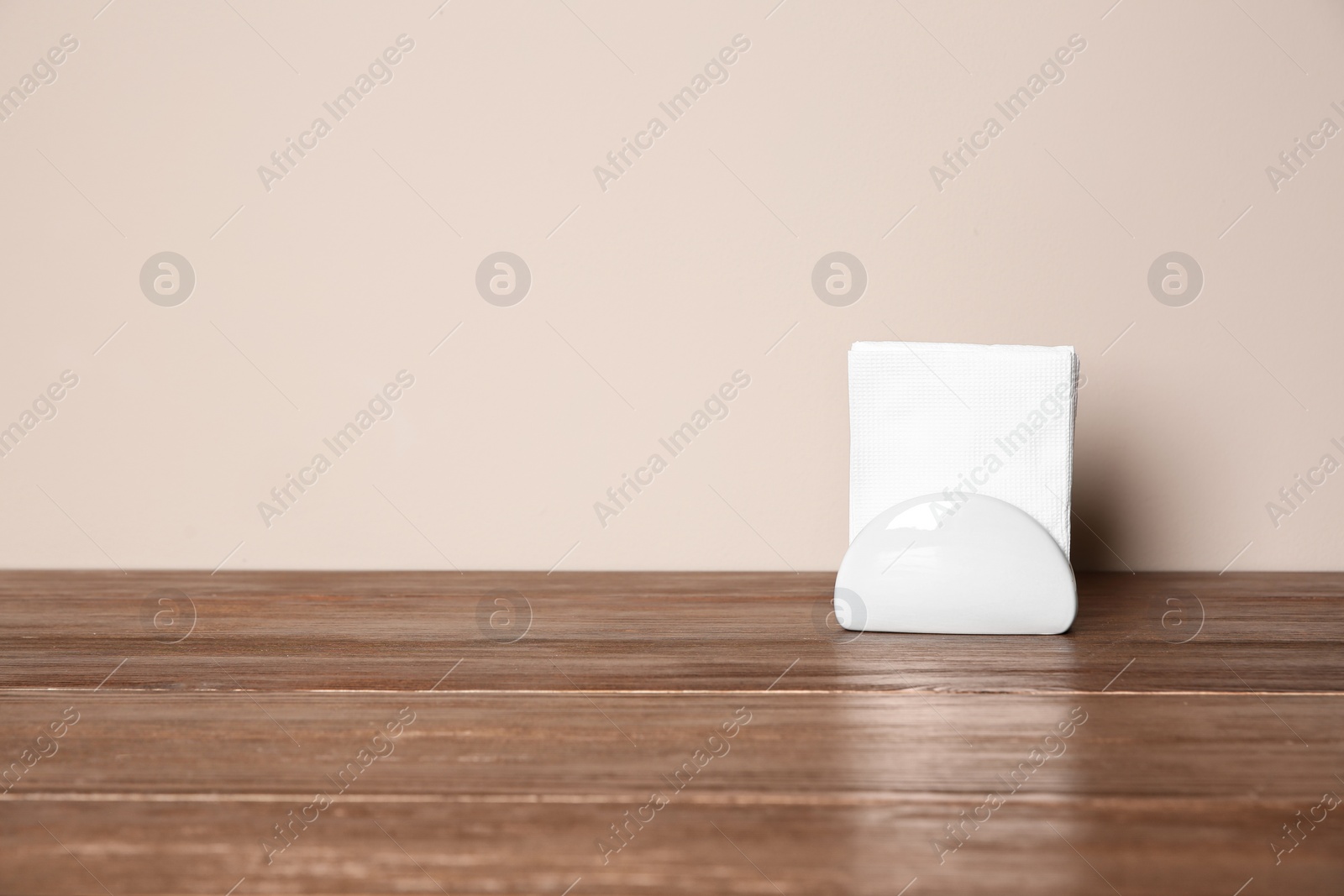 Photo of Napkin holder with paper serviettes on table against color background. Space for text