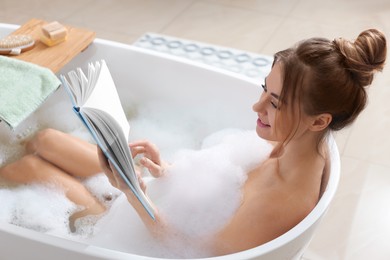 Beautiful woman reading book while enjoying bubble bath at home