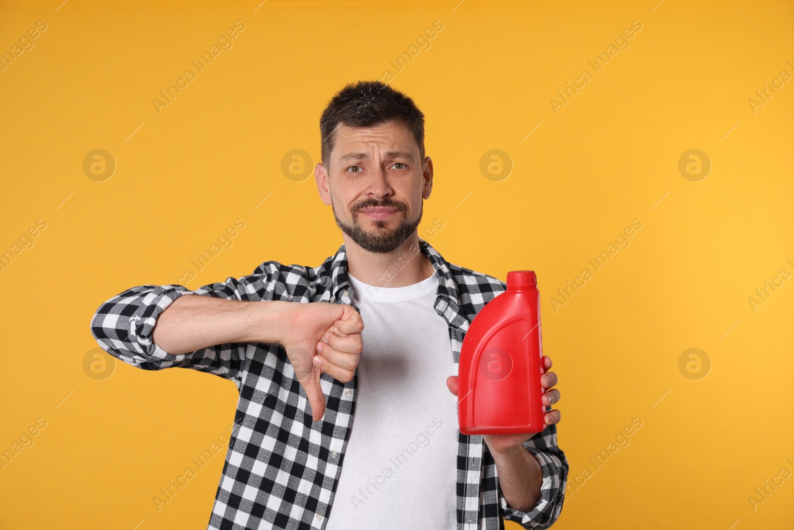 Photo of Man holding red container of motor oil and showing thumbs down on orange background