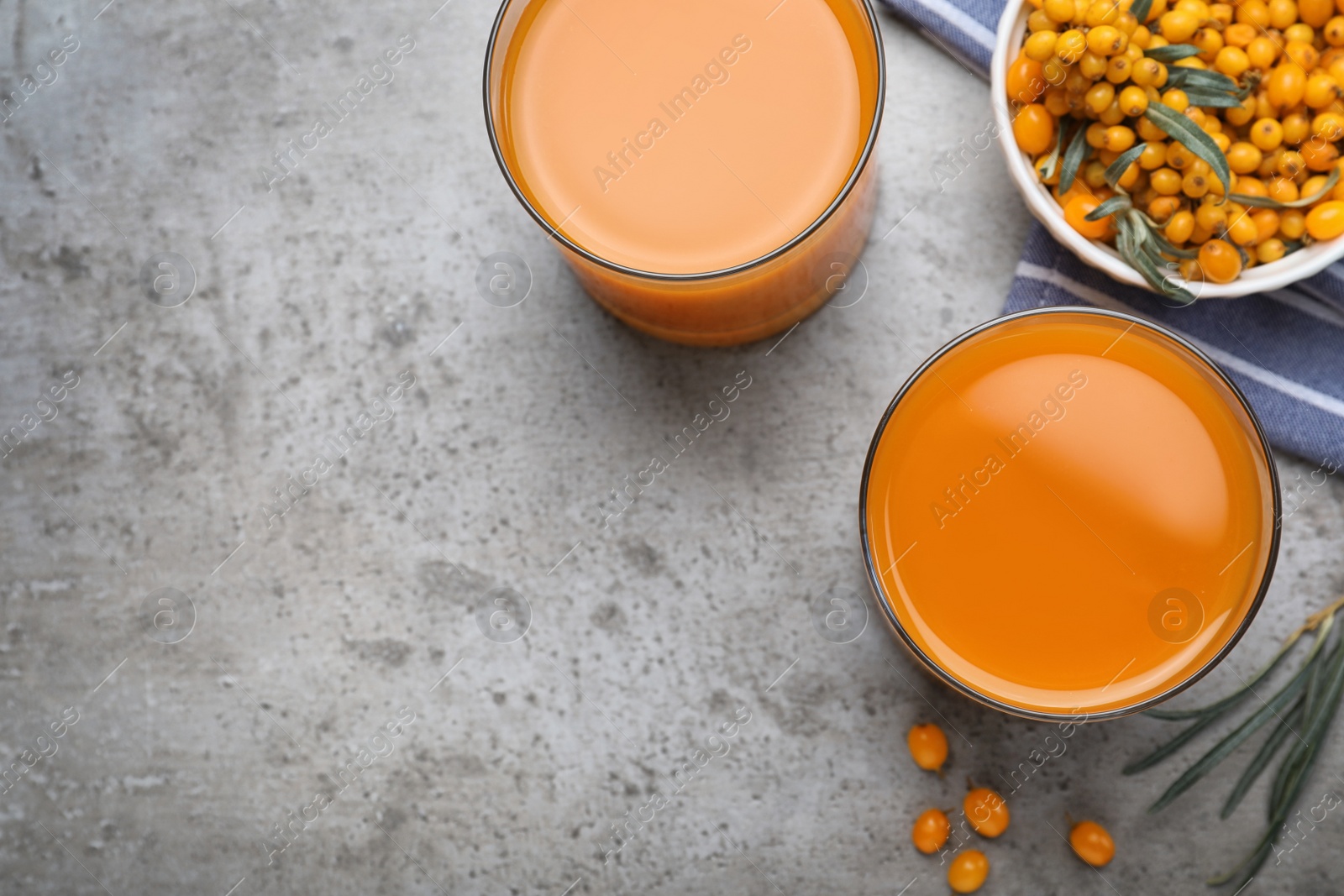 Photo of Delicious sea buckthorn juice and fresh berries on grey table, top view. Space for text