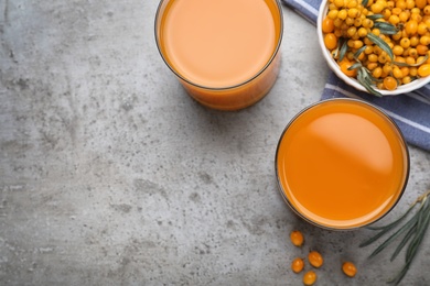 Delicious sea buckthorn juice and fresh berries on grey table, top view. Space for text