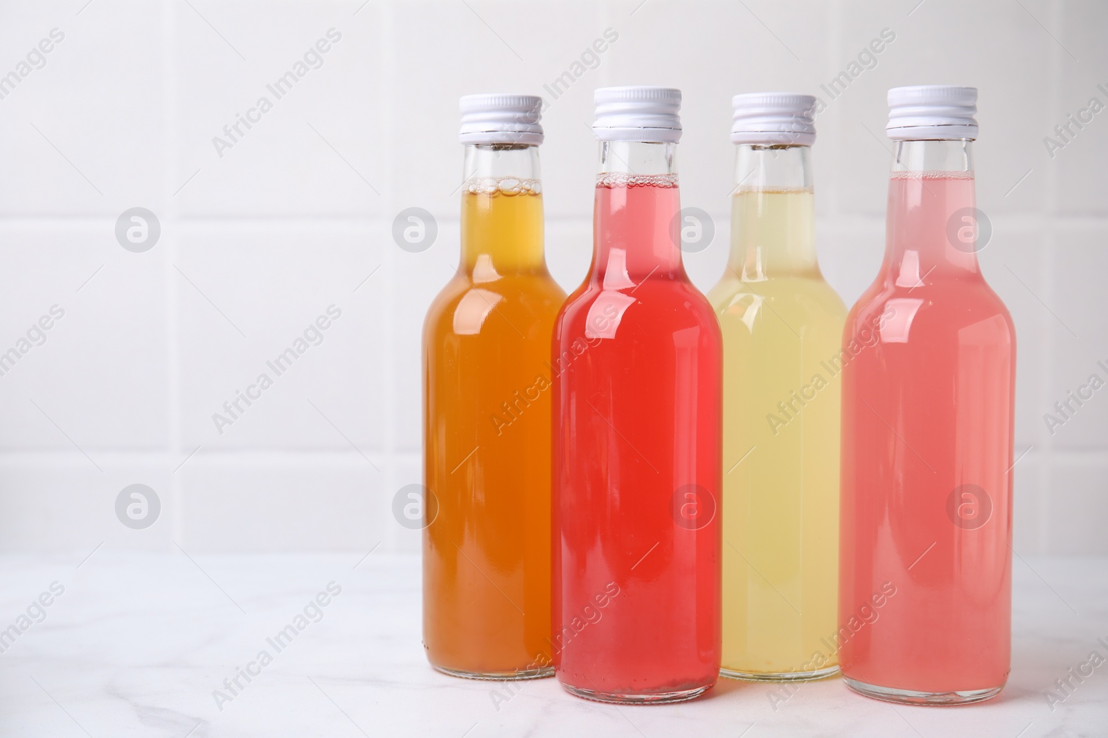 Photo of Delicious kombucha in glass bottles on white marble table, space for text