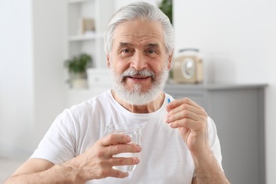 Photo of Senior man with glass of water and pill at home