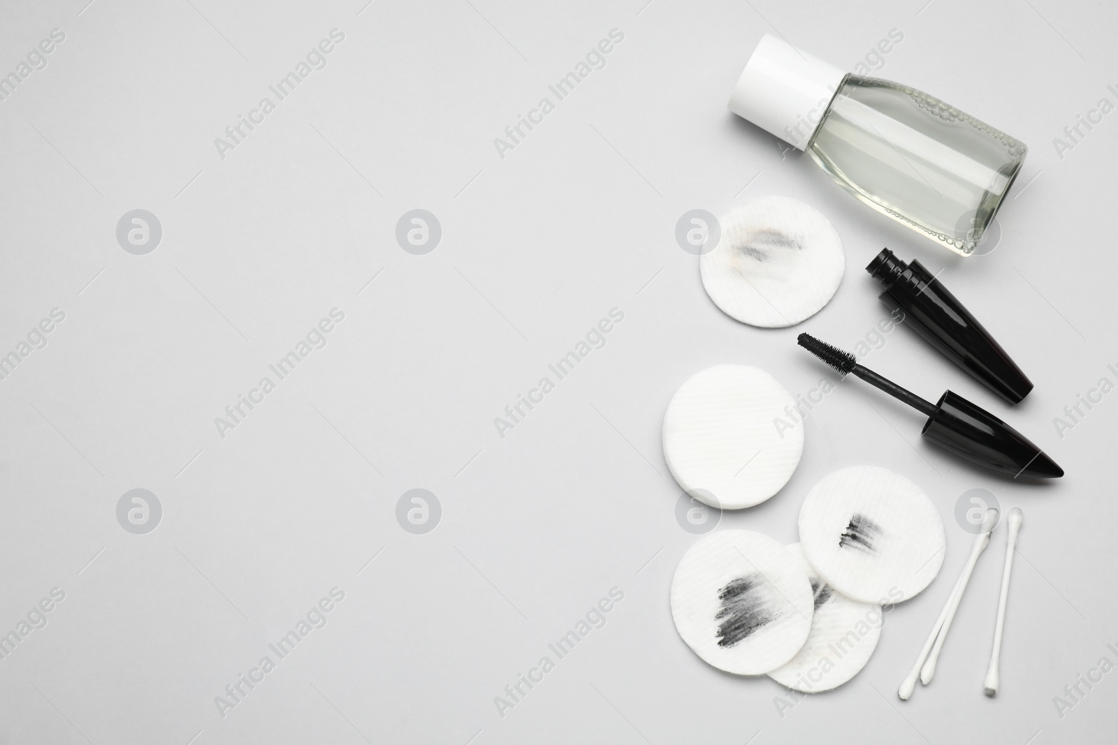 Photo of Bottle of makeup remover, mascara, cotton pads and buds on light grey background, flat lay. Space for text