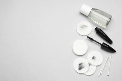 Bottle of makeup remover, mascara, cotton pads and buds on light grey background, flat lay. Space for text