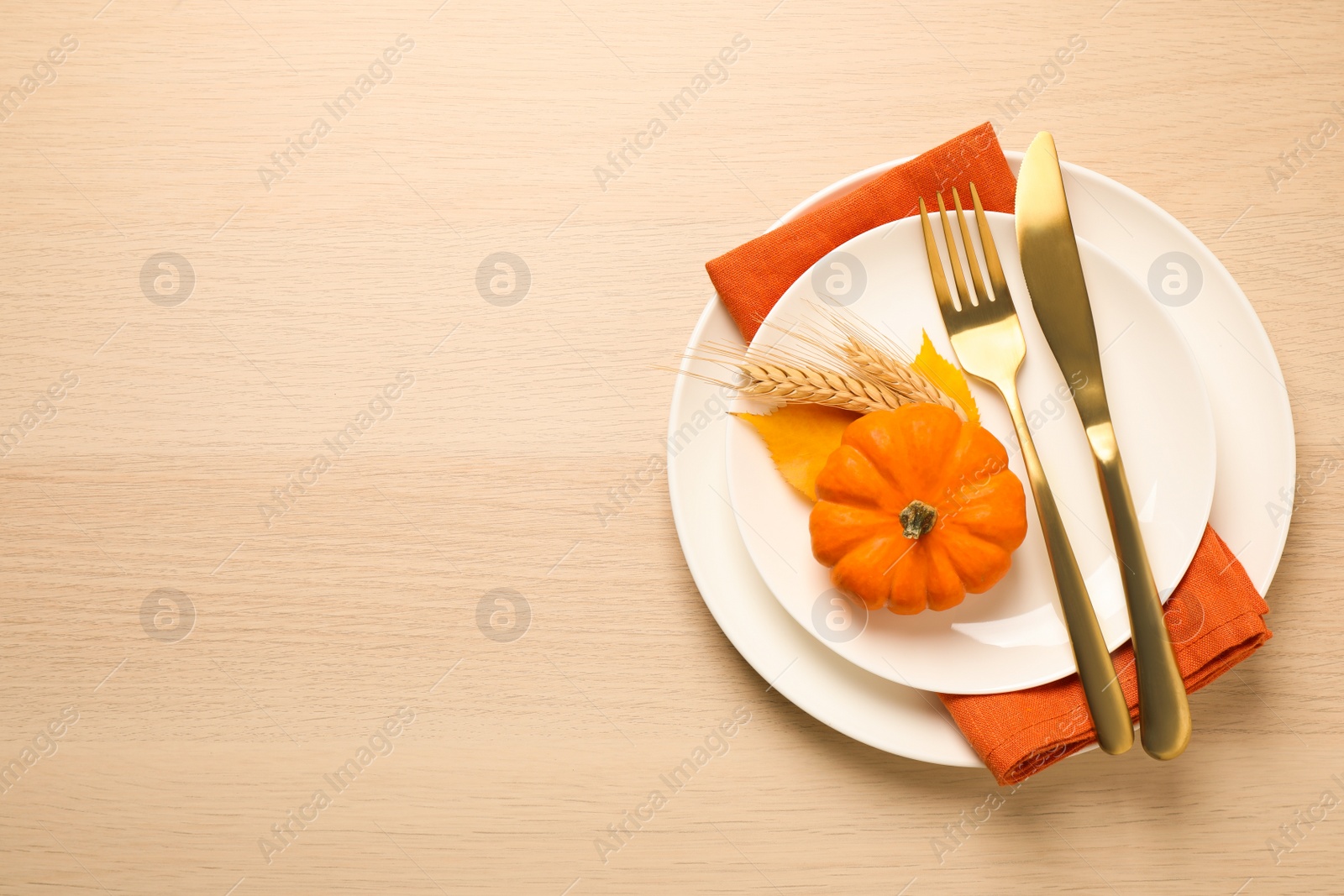 Photo of Top view of seasonal table setting with autumn leaves, pumpkin and wheat spikes on wooden background, space for text. Thanksgiving Day