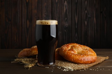 Photo of Tasty pretzels, glass of beer and wheat spikes on wooden table