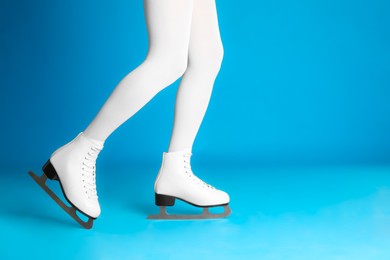 Photo of Woman in elegant white ice skates on light blue background, closeup of legs. Space for text