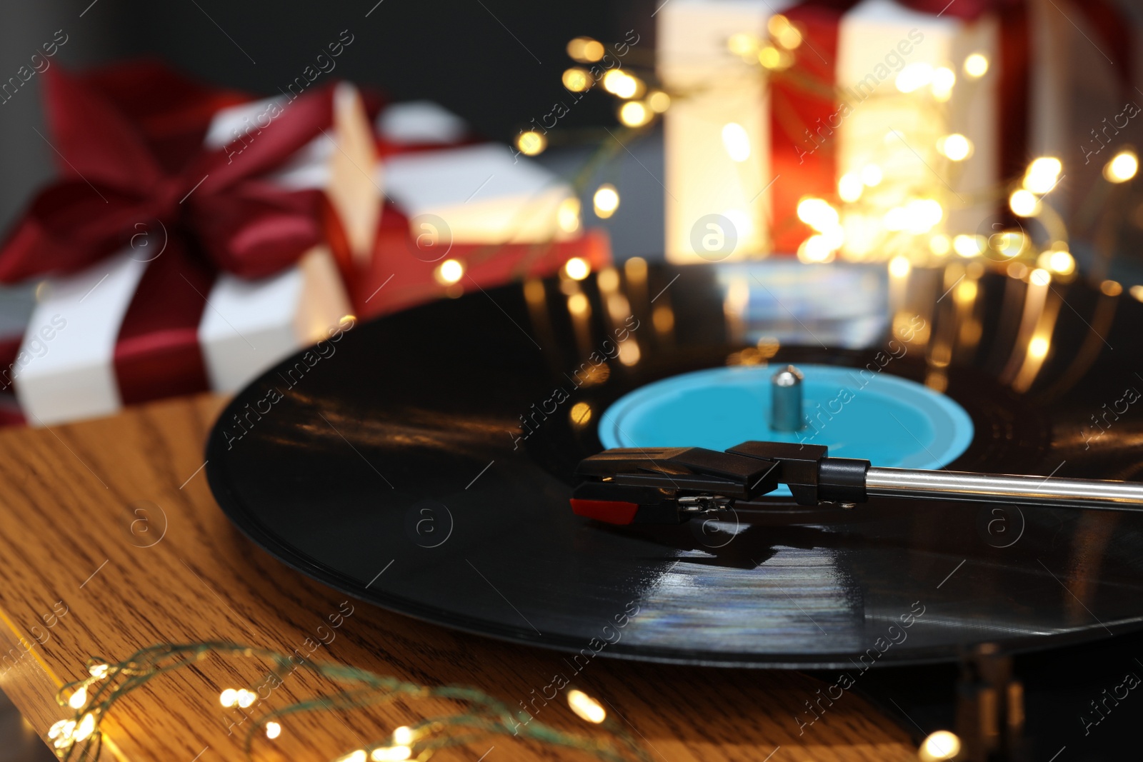 Photo of Turntable with vinyl record, fairy lights and Christmas gift boxes, closeup