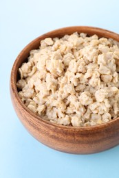 Photo of Tasty boiled oatmeal in bowl on light blue background, closeup