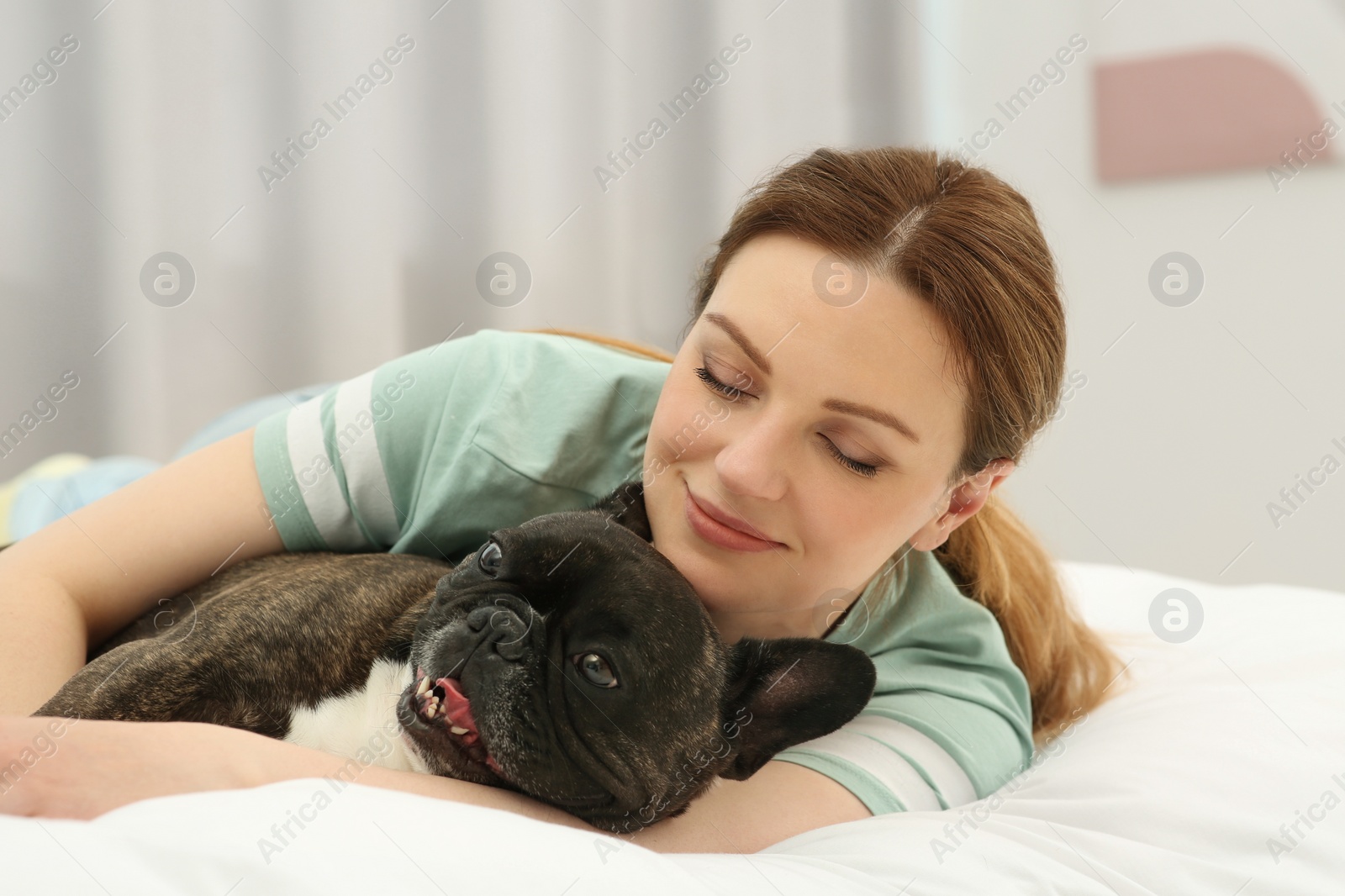 Photo of Happy woman hugging cute French Bulldog on bed in room