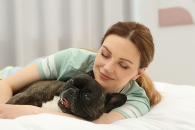 Happy woman hugging cute French Bulldog on bed in room