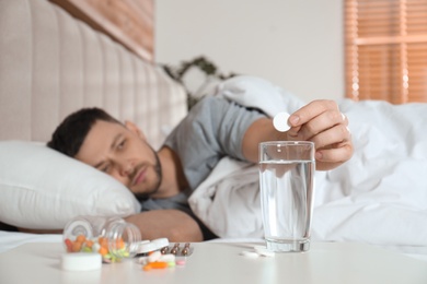 Man taking medicine for hangover in bed at home, focus on hand with pill