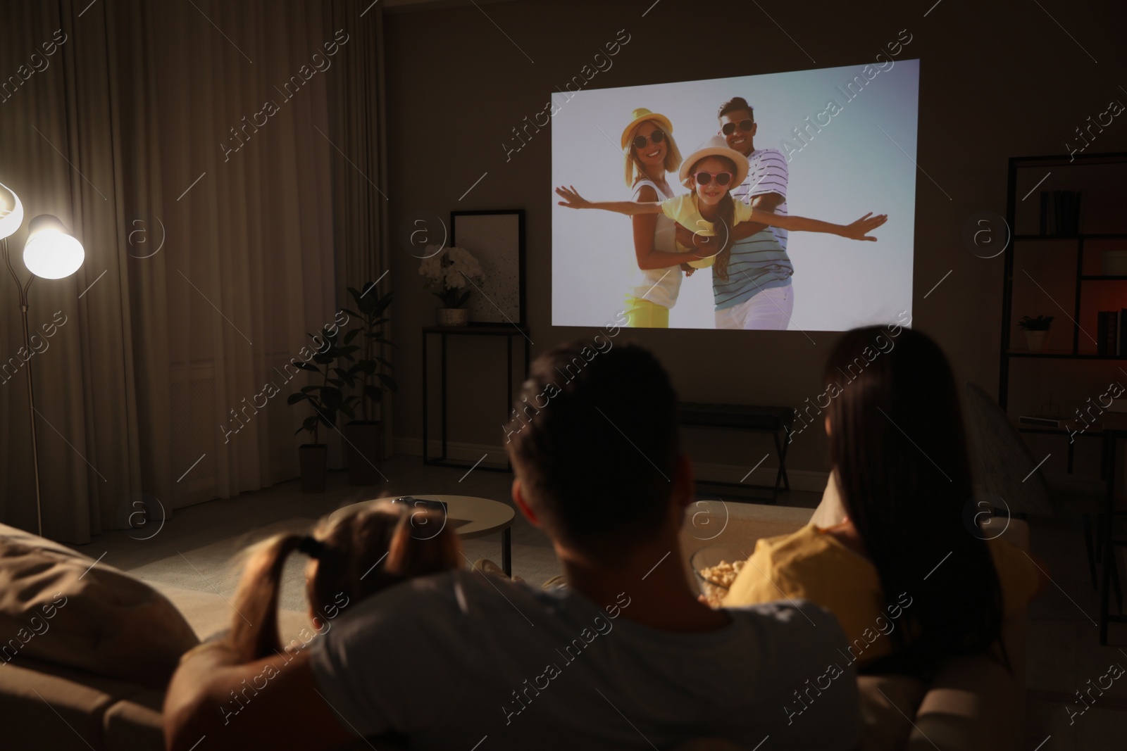 Photo of Family watching movie on sofa at night, back view