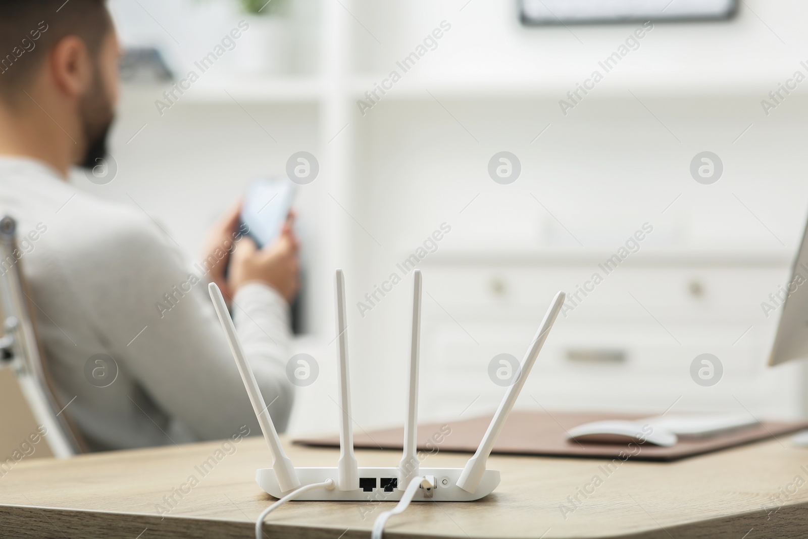 Photo of Man with smartphone working at wooden table indoors, focus on Wi-Fi router