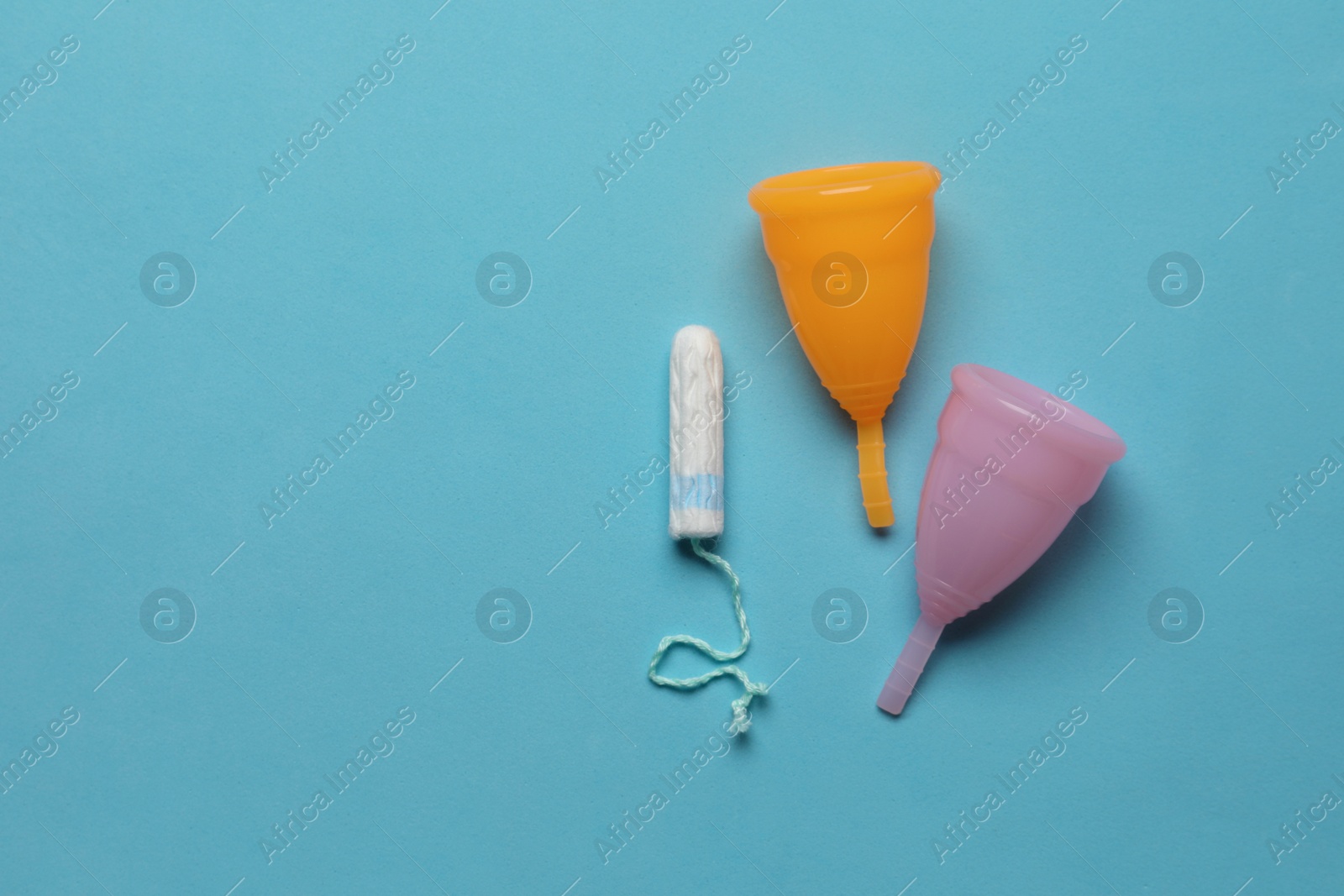 Photo of Menstrual cups near tampon on light blue background, flat lay with space for text. Reusable and disposable feminine products