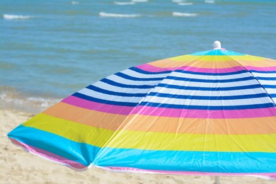 Photo of Colorful striped umbrella on beach near sea, closeup
