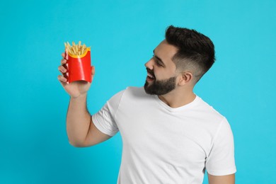 Young man with French fries on light blue background