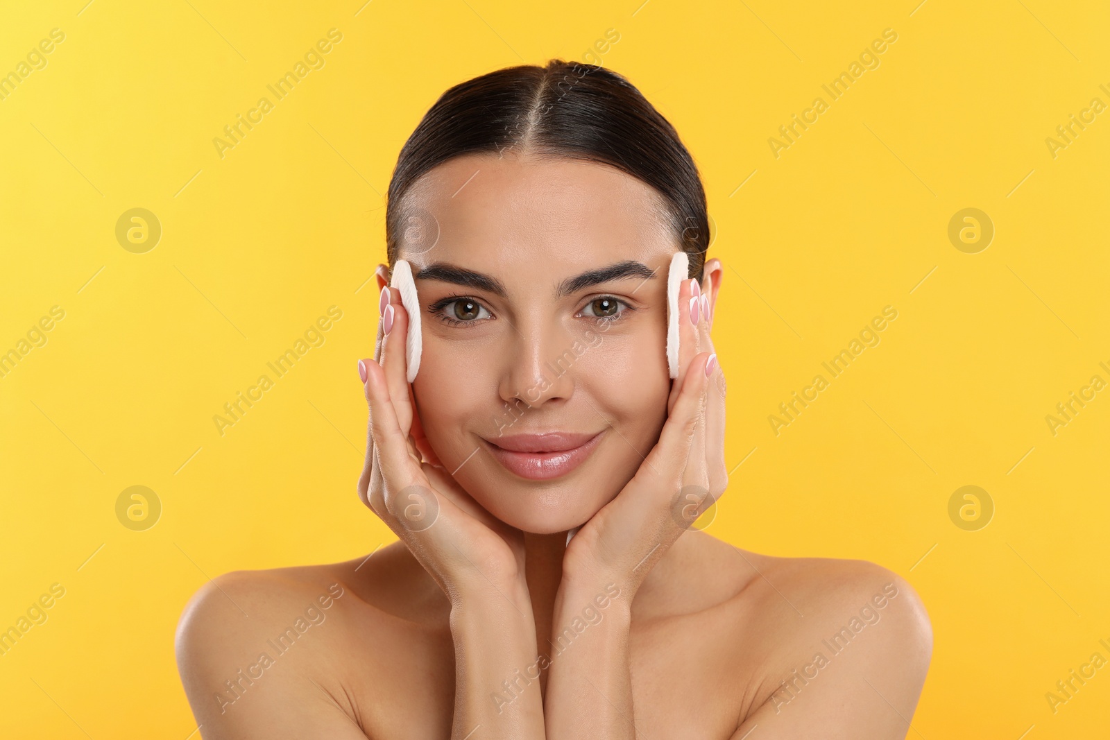 Photo of Beautiful woman removing makeup with cotton pads on yellow background