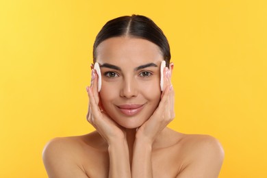 Beautiful woman removing makeup with cotton pads on yellow background