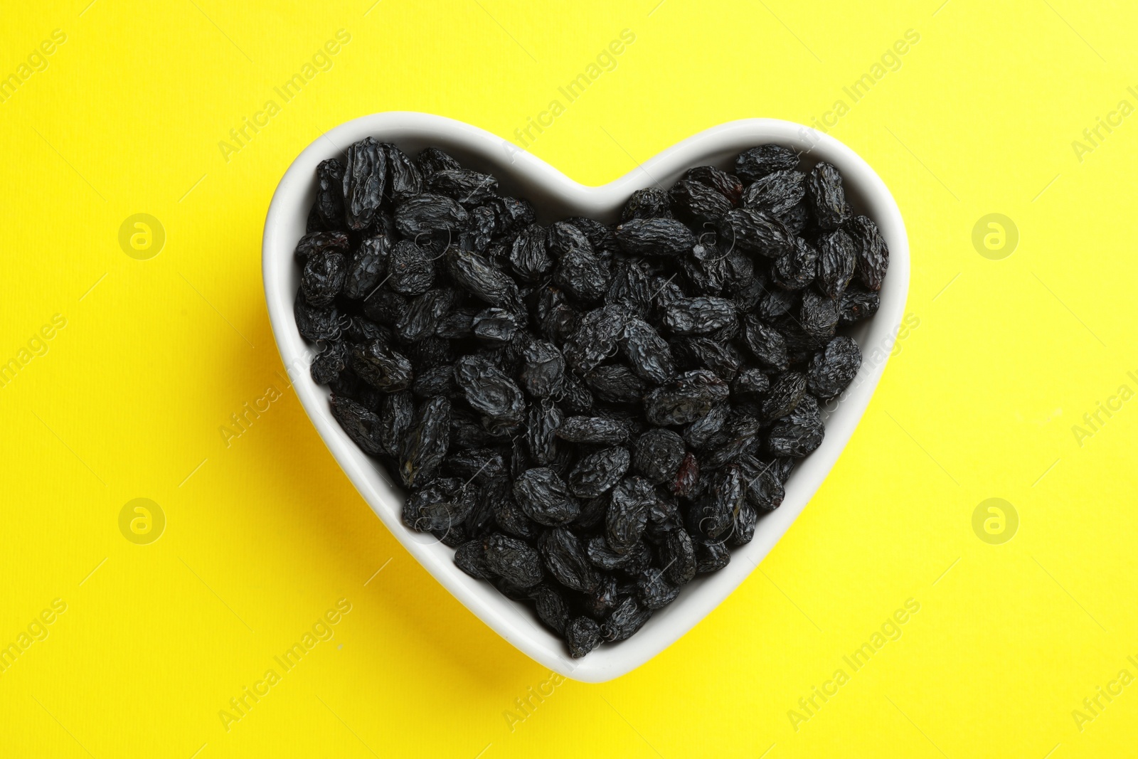 Photo of Heart shaped plate with raisins on color background, top view. Dried fruit as healthy snack