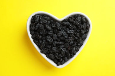 Photo of Heart shaped plate with raisins on color background, top view. Dried fruit as healthy snack