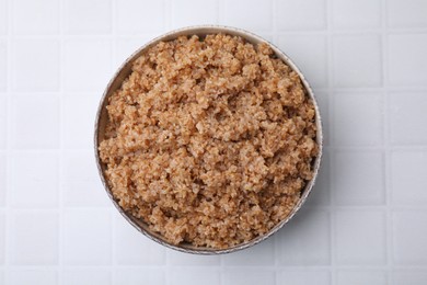 Tasty wheat porridge in bowl on white tiled table, top view