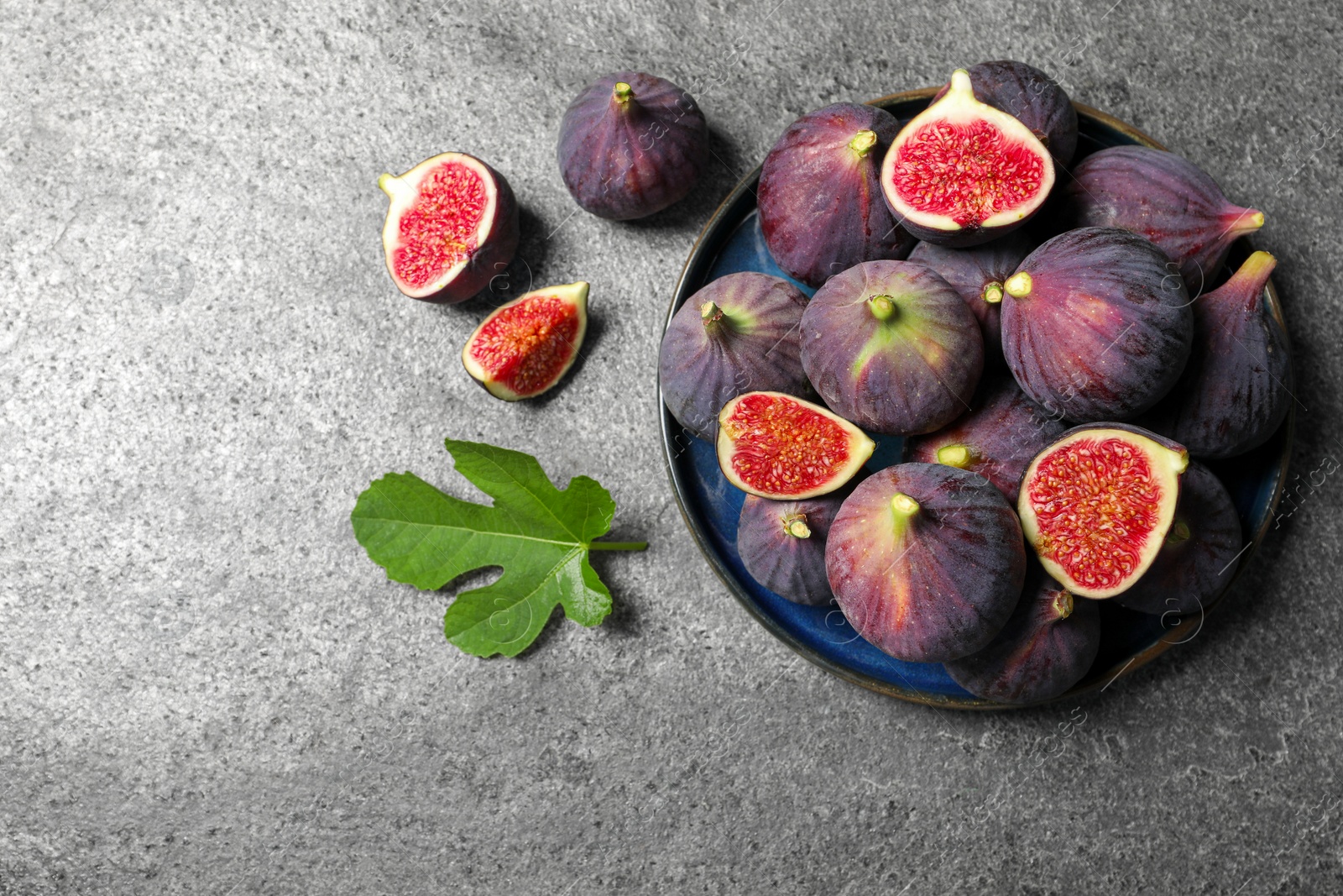 Photo of Whole and cut ripe figs with leaf on light grey textured table, flat lay. Space for text