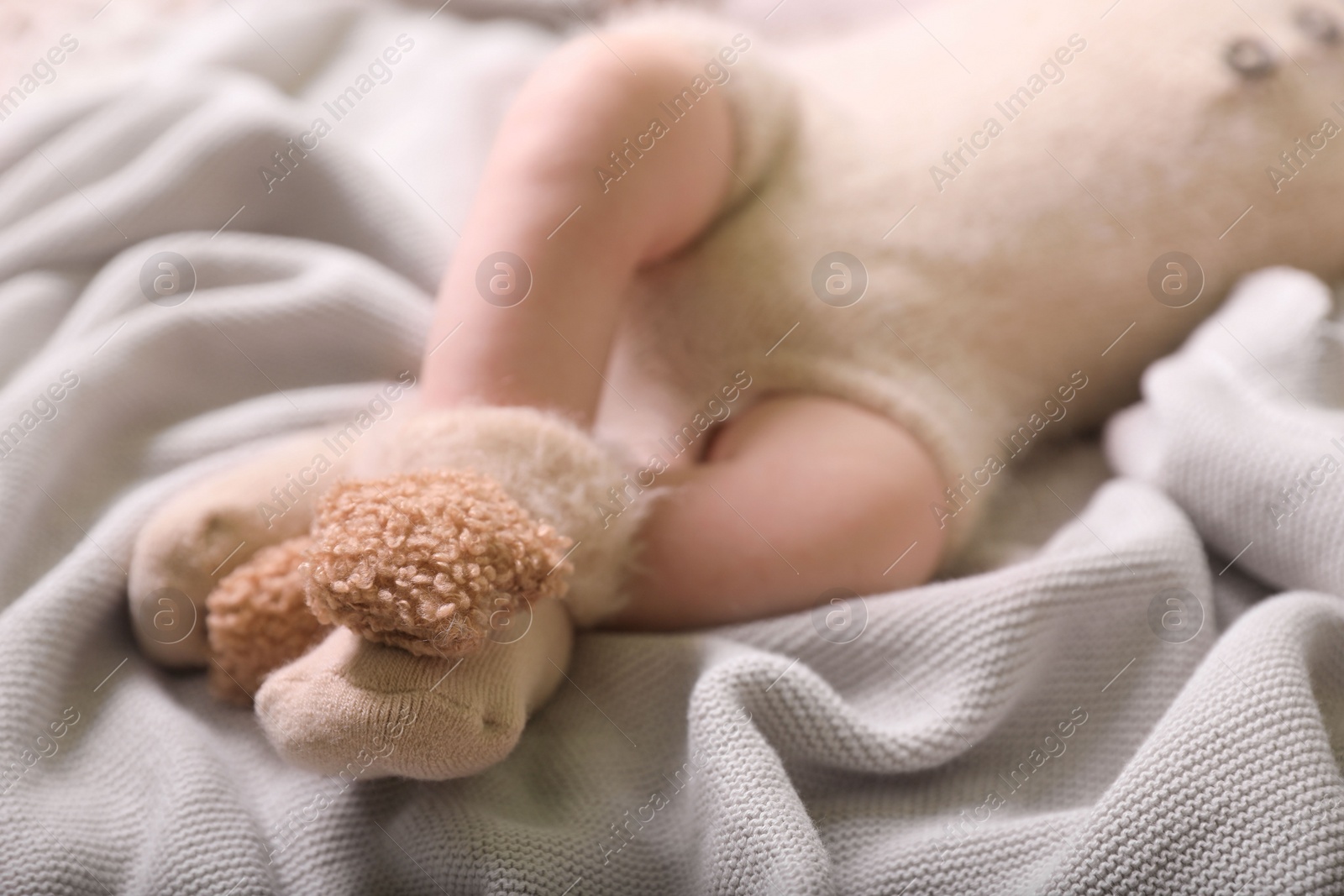 Photo of Cute newborn baby in knitted booties lying on light grey plaid, closeup of legs