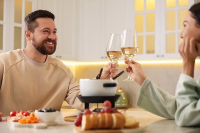 Photo of Romantic date with fondue. Couple clinking glasses of wine at home