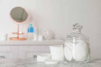 Glass jar with cotton pads for removing makeup on white marble table in bathroom