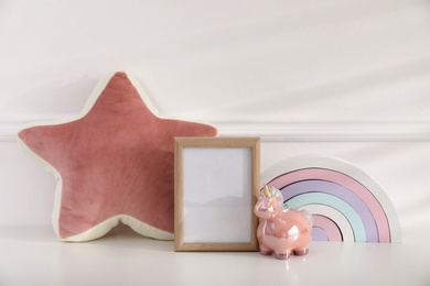 Photo of Empty photo frame, cute toy unicorn and pillow near wall, space for text. Baby room interior element