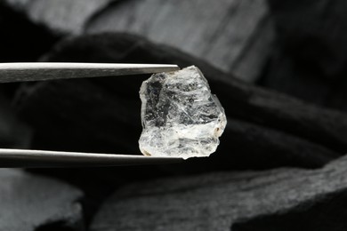 Photo of Tweezers with shiny rough diamond over coal, closeup