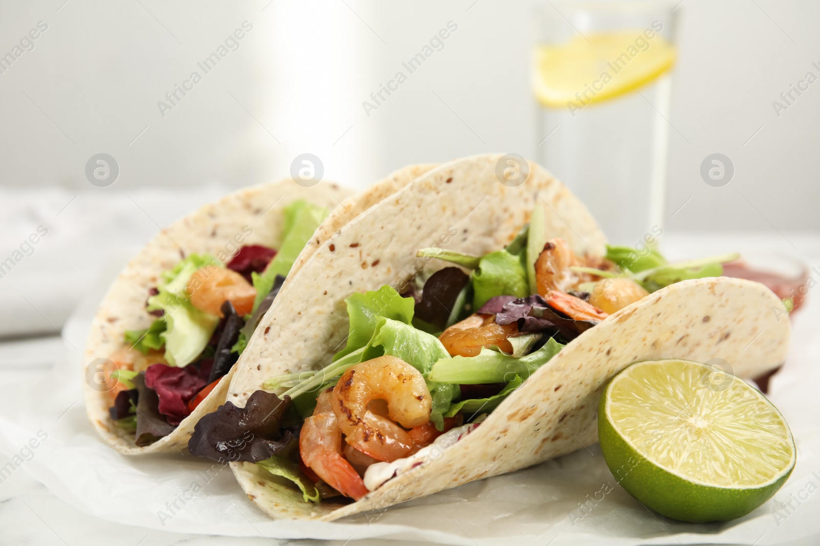 Photo of Delicious tacos with shrimps and lime on white table, closeup