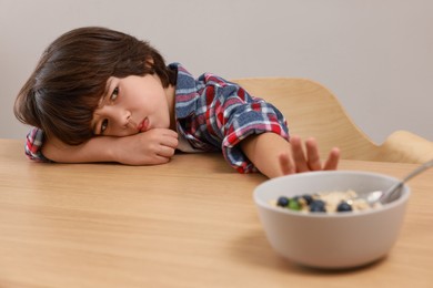 Cute little boy refusing to eat his breakfast at table on grey background