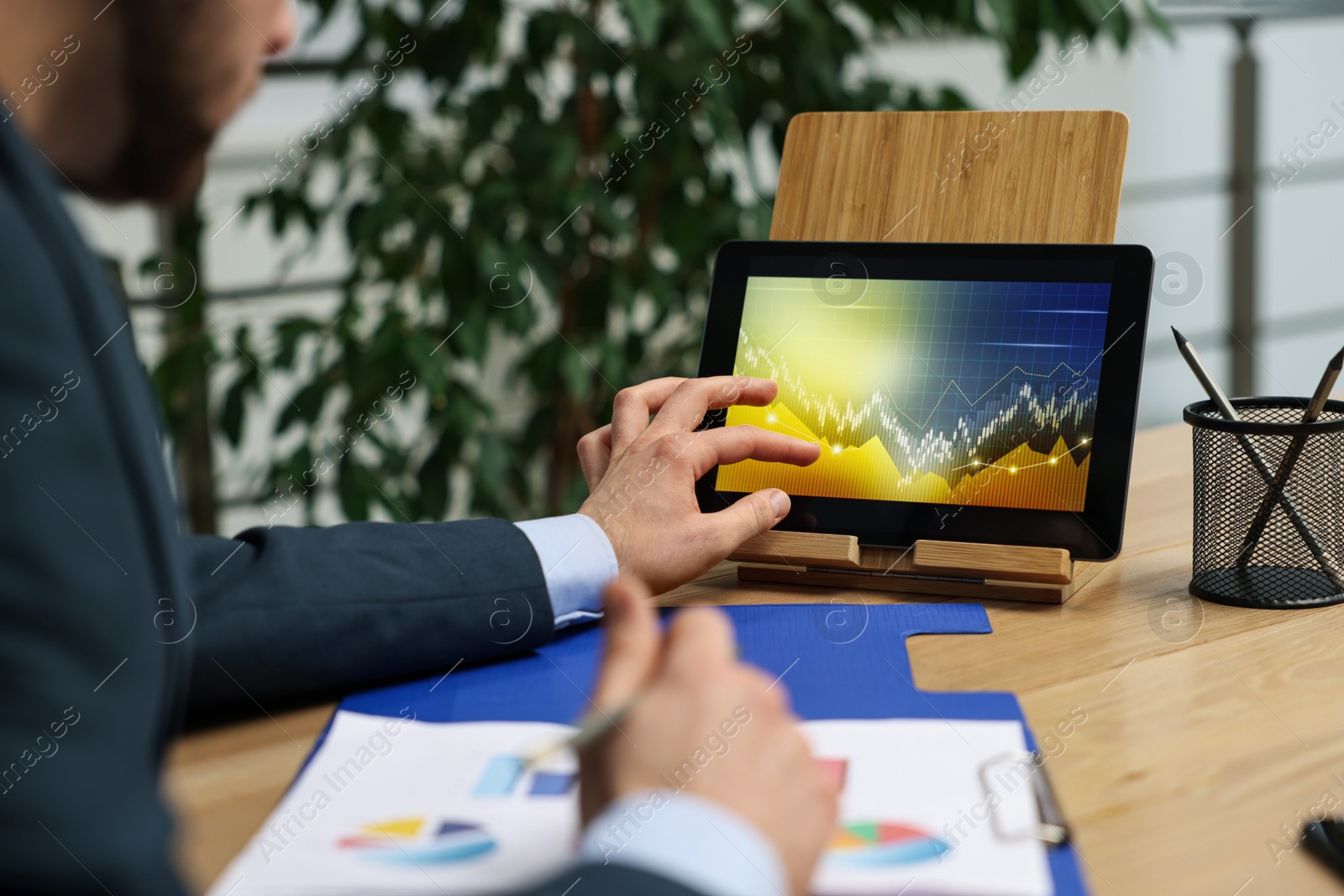 Photo of Broker working with tablet and charts at table in office, closeup. Forex trading