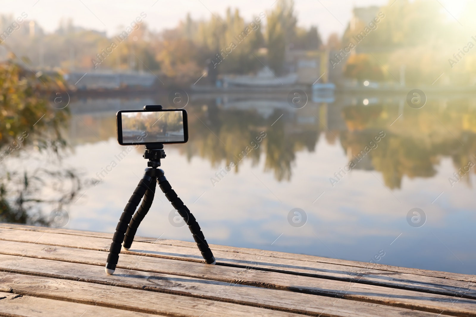 Photo of Tripod with smartphone on wooden pier near river
