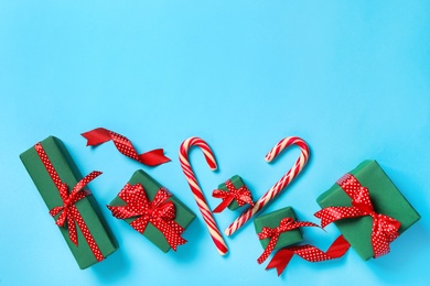 Photo of Christmas gift boxes with red bows and candy canes on light blue background, flat lay. Space for text