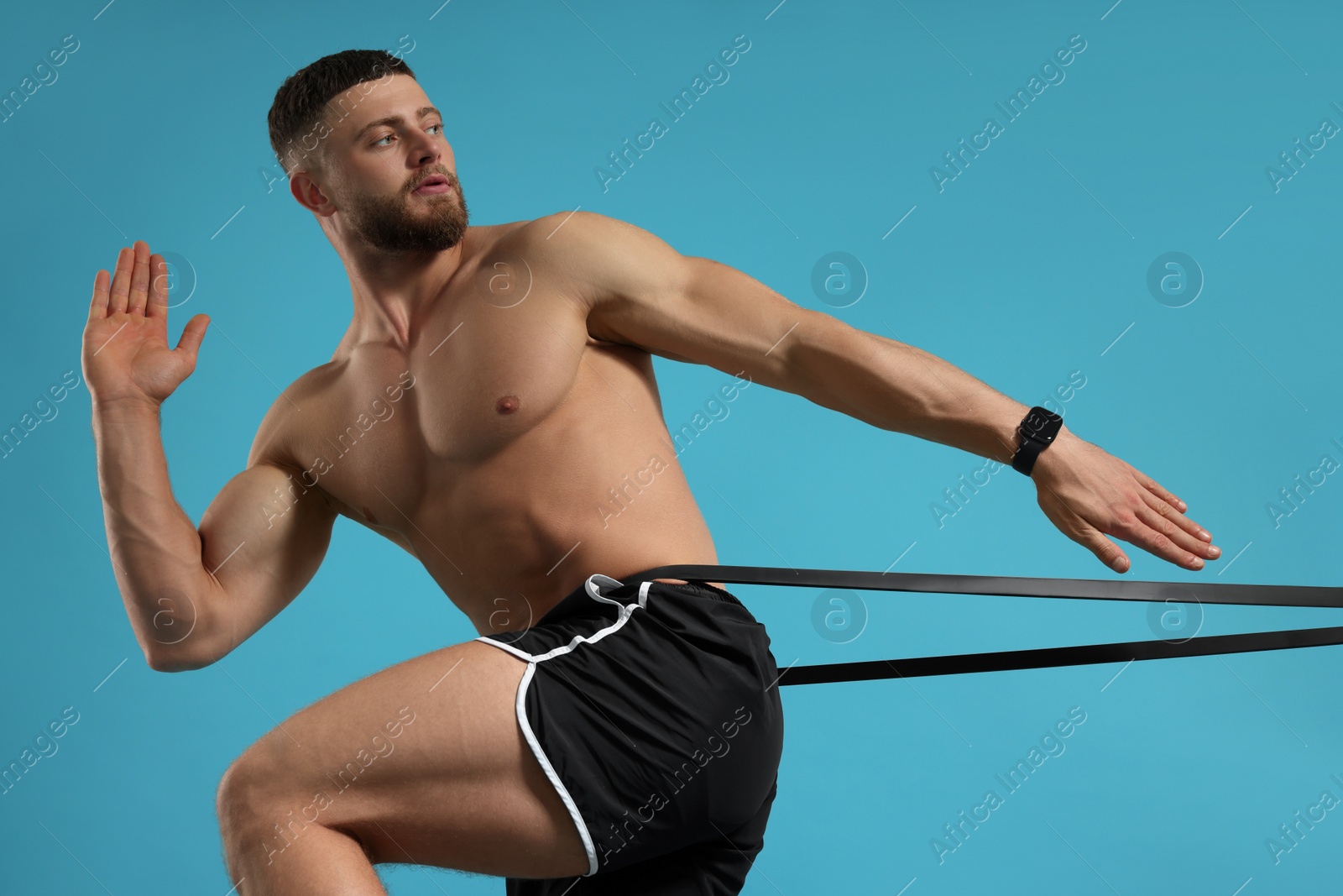 Photo of Muscular man exercising with elastic resistance band on light blue background