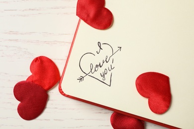 Notebook with text I Love You and red hearts on white wooden table, flat lay