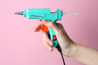 Photo of Woman holding turquoise glue gun with stick on pink background, closeup