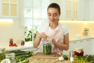 Photo of Woman putting bay leaves into pickling jar at table in kitchen