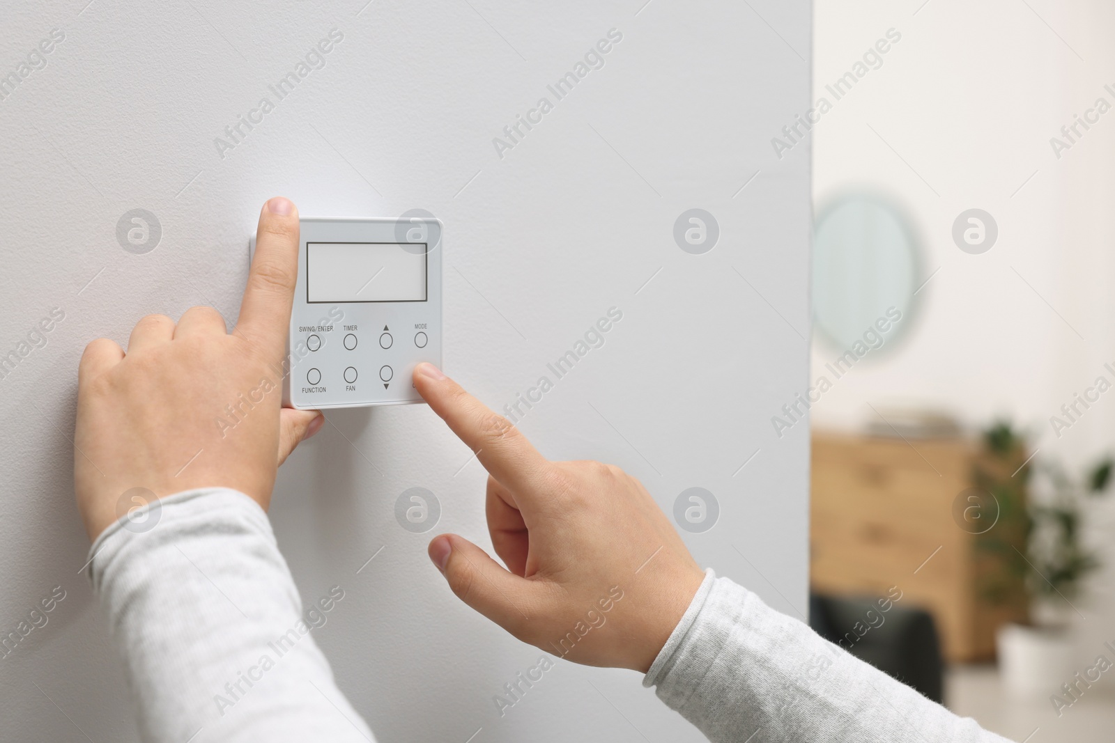 Photo of Woman adjusting thermostat on white wall indoors, closeup. Smart home system