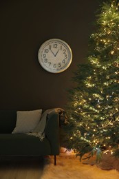 Beautiful Christmas tree with golden lights, couch and clock on wall in living room