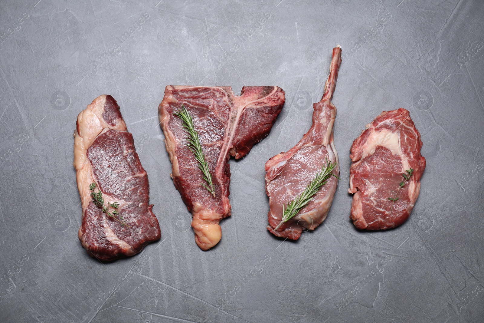 Photo of Fresh raw beef cuts with herbs on light grey textured table, flat lay